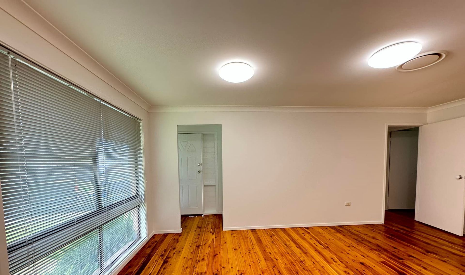 An Empty Living Room With Hardwood Floors and White Walls — JAX Painting Services in Central Coast, NSW