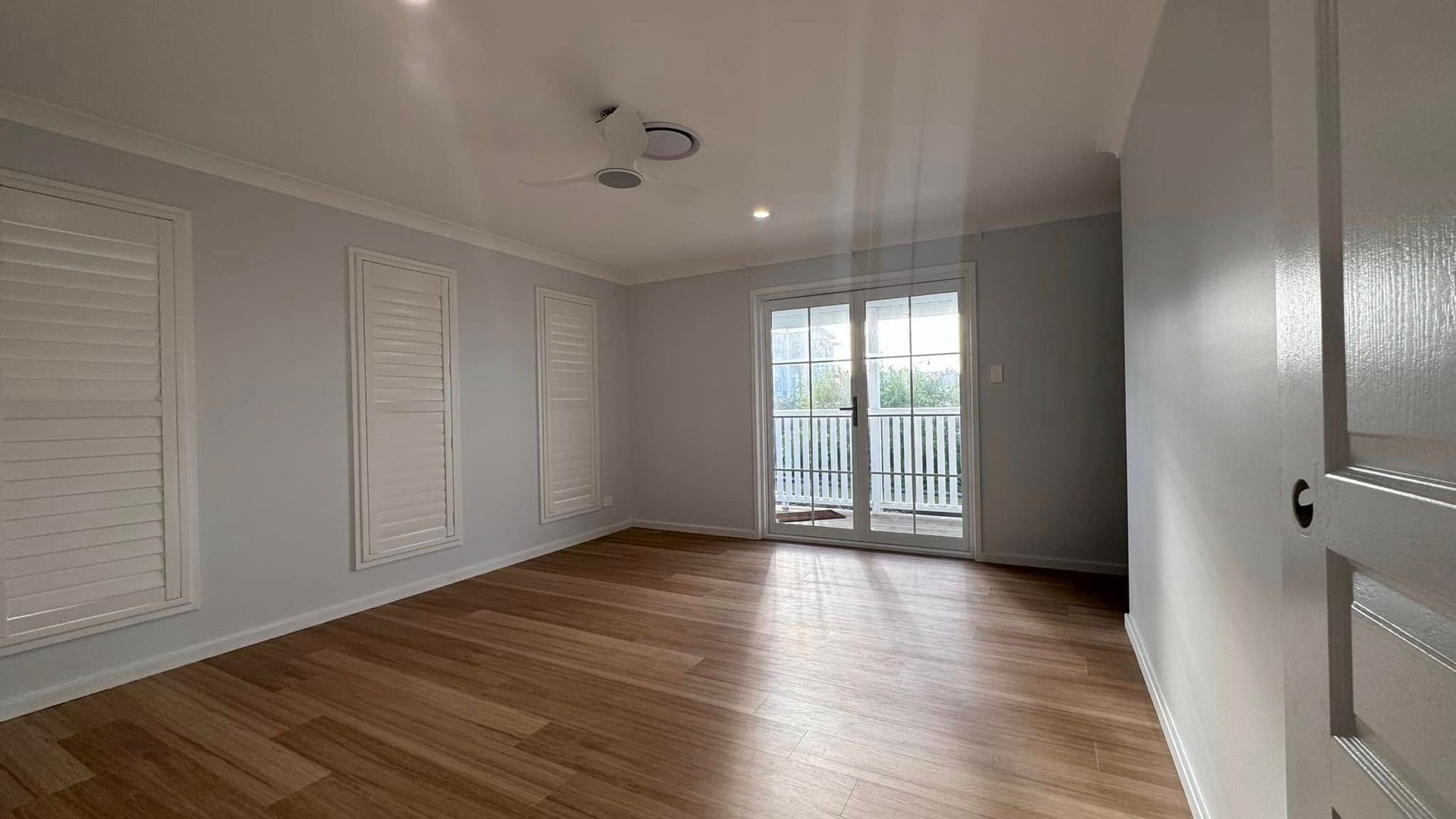 An Empty Room With Hardwood Floors, White Walls and Sliding Glass Doors — JAX Painting Services in Central Coast, NSW