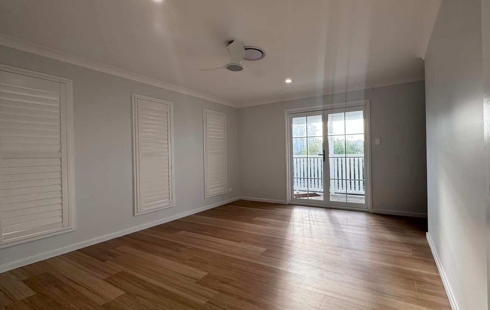 An Empty Living Room With Hardwood Floors, White Shutters and a Ceiling Fan — JAX Painting Services in Central Coast, NSW