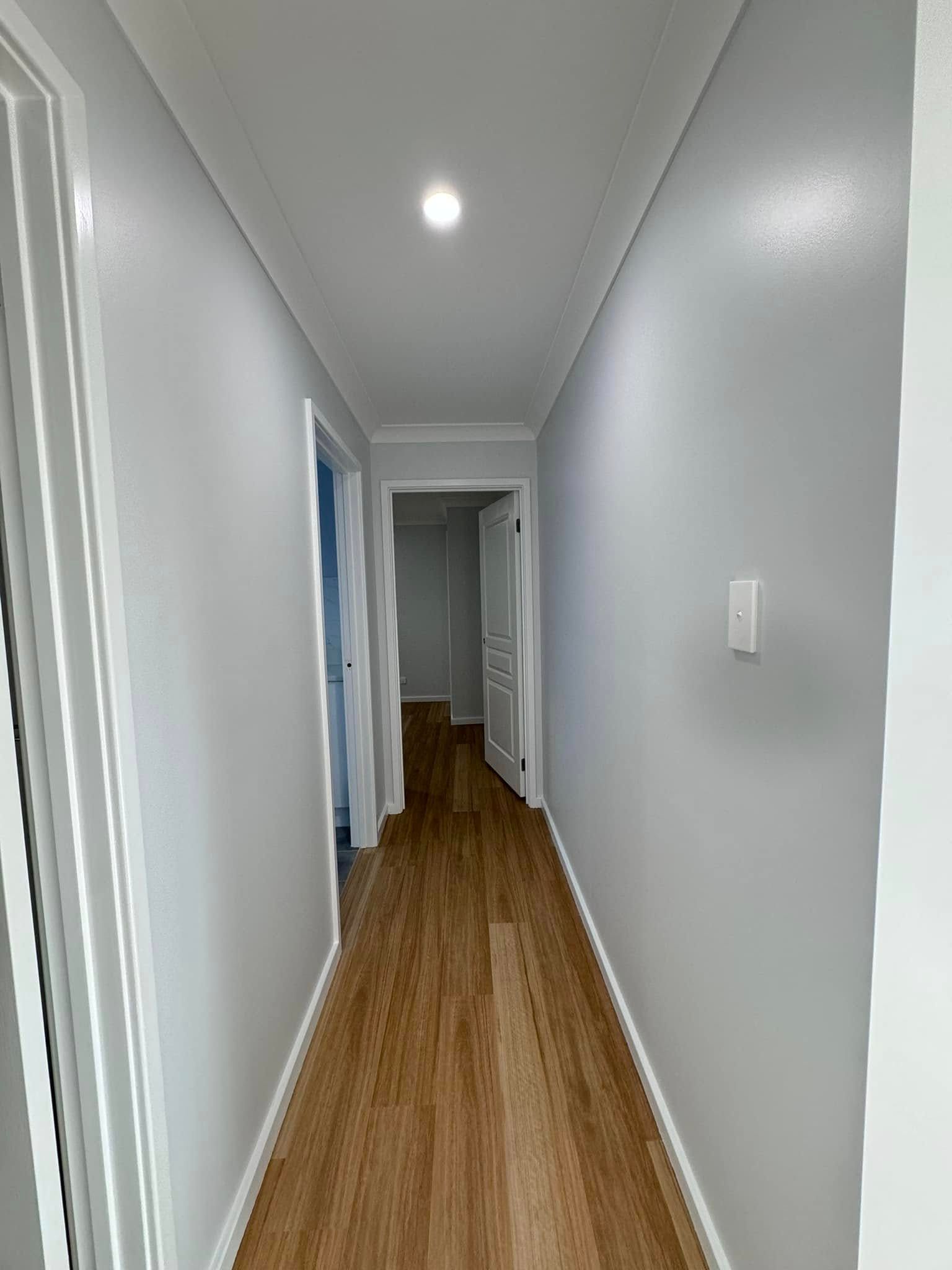 A Long Hallway With Hardwood Floors and White Walls in a House — JAX Painting Services in Central Coast, NSW