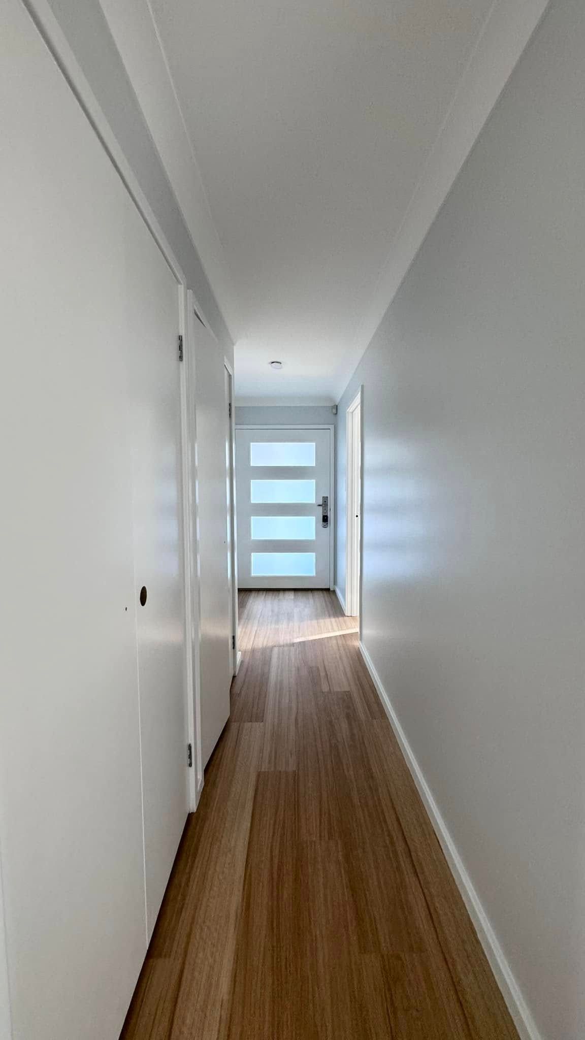 A Long Hallway With Wooden Floors and White Walls Leading to a Door — JAX Painting Services in Central Coast, NSW