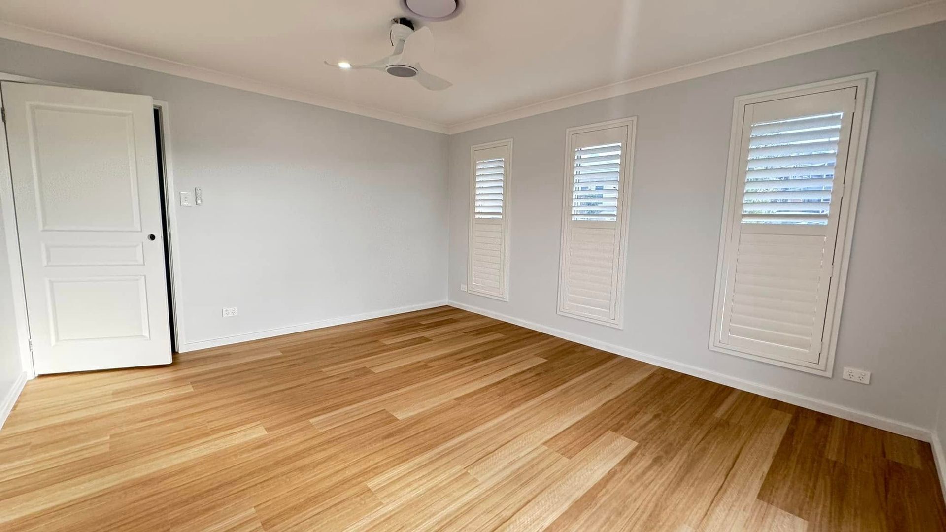 An Empty Room With Hardwood Floors, White Shutters and a Ceiling Fan — JAX Painting Services in Central Coast, NSW