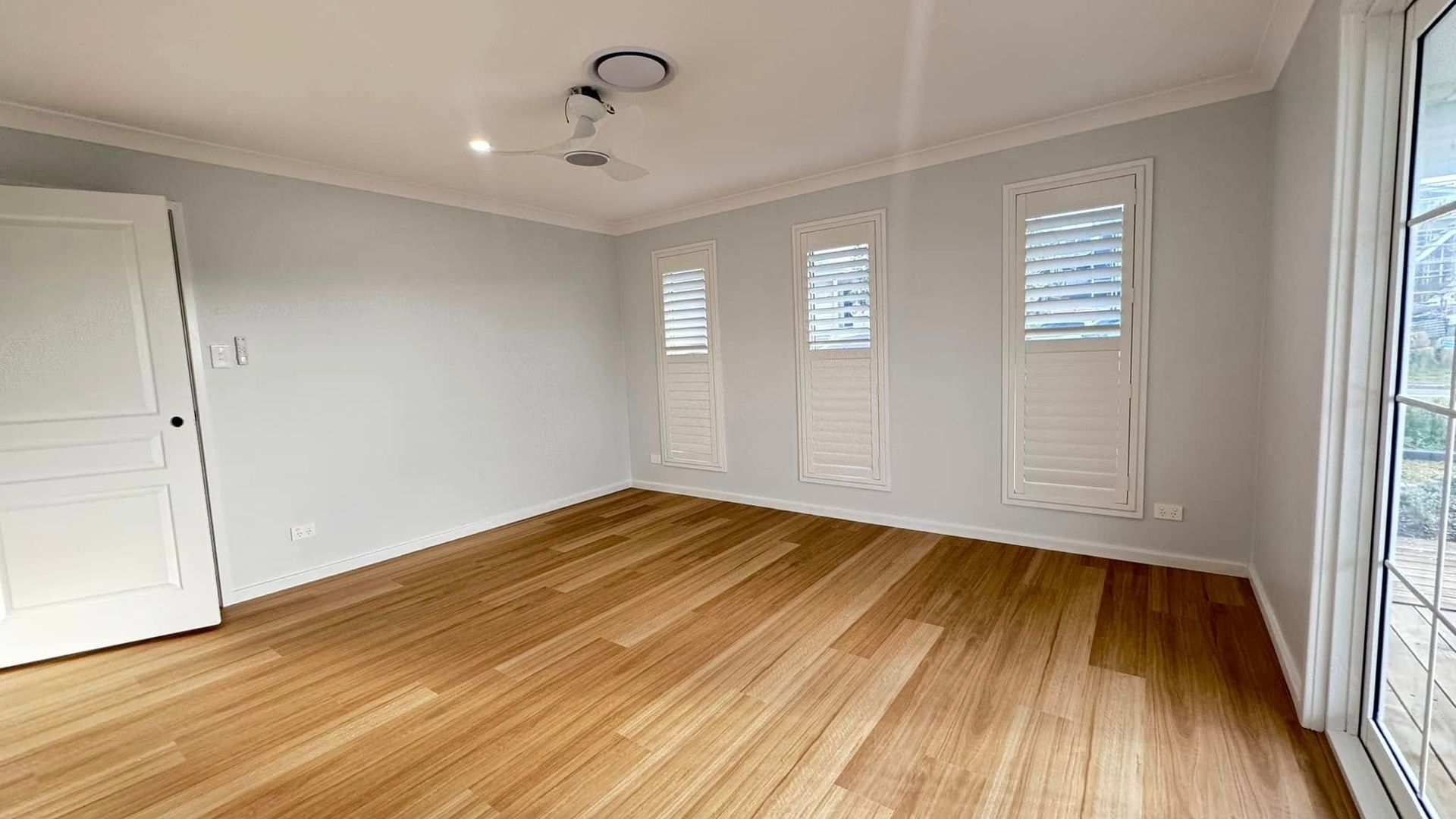 An Empty Room With Hardwood Floors and White Shutters on the Windows — JAX Painting Services in Central Coast, NSW