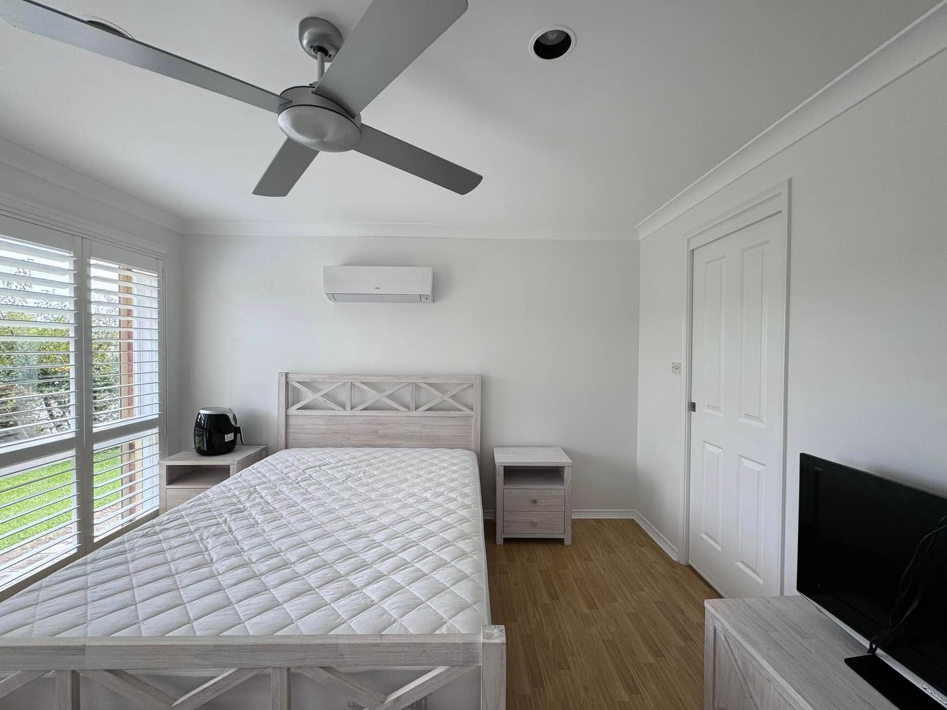 A Bedroom With a Bed, Nightstand, Television and Ceiling Fan — JAX Painting Services in Central Coast, NSW