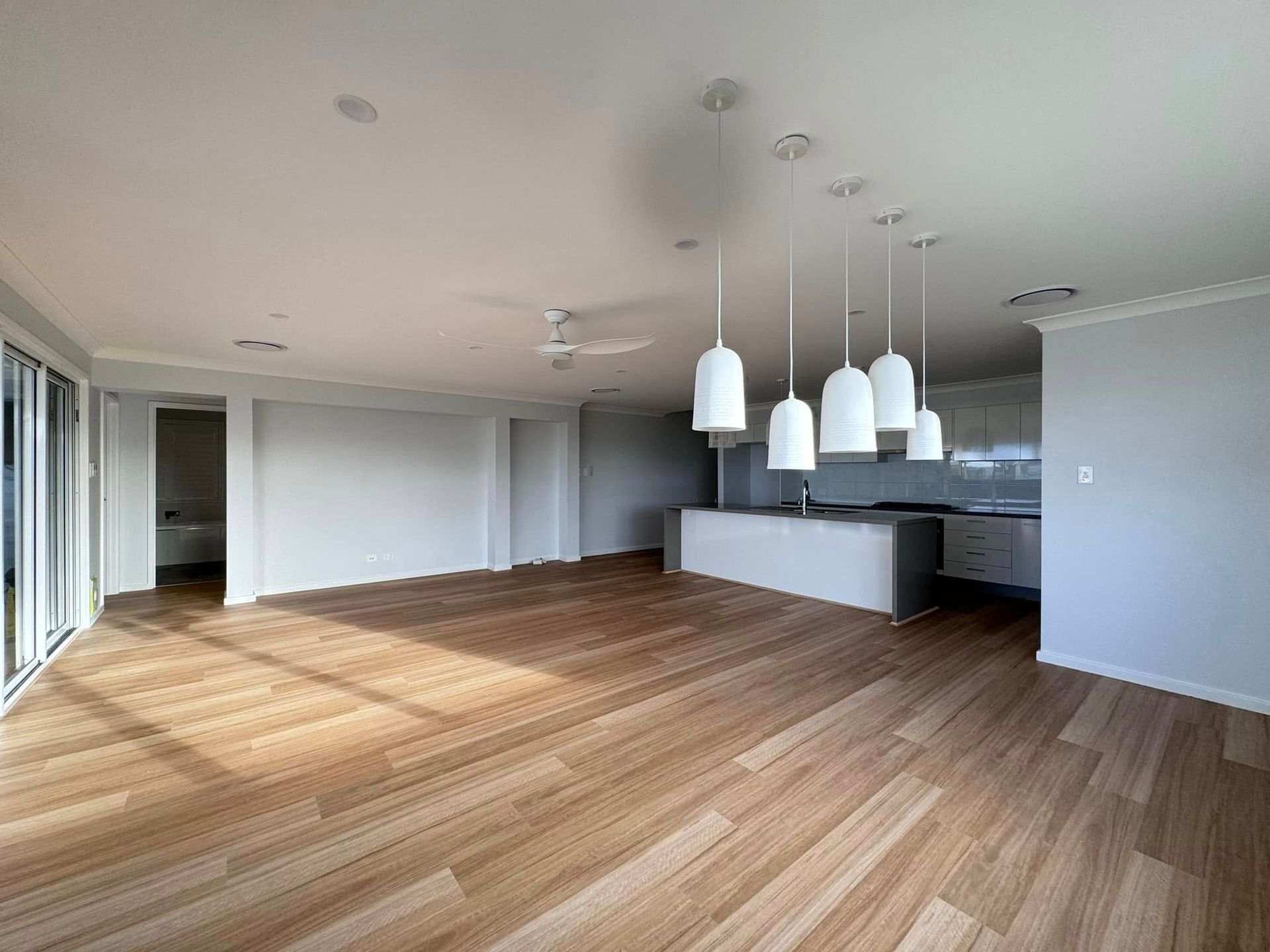 An Empty Living Room With Hardwood Floors and a Kitchen — JAX Painting Services in Central Coast, NSW