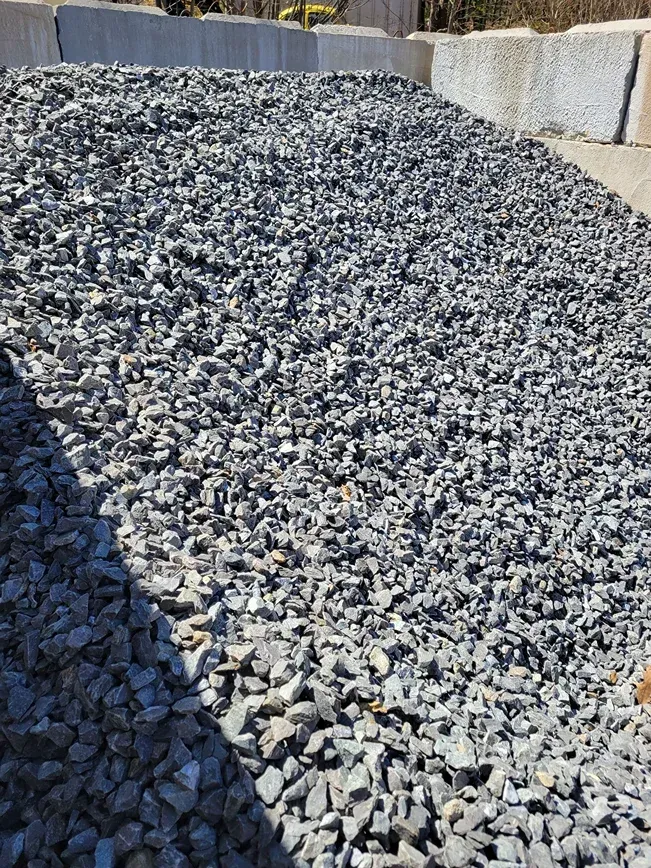 A pile of dark gray crushed stone or gravel situated against concrete retaining wall blocks.
