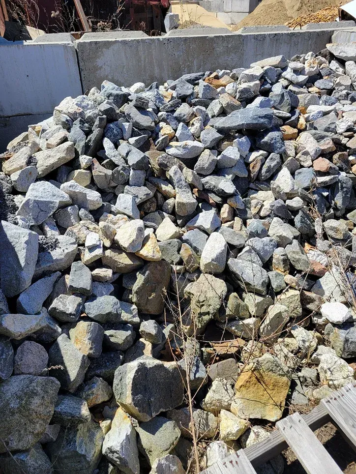 Pile of gray and tan rocks and rubble stacked outdoors against a concrete barrier
