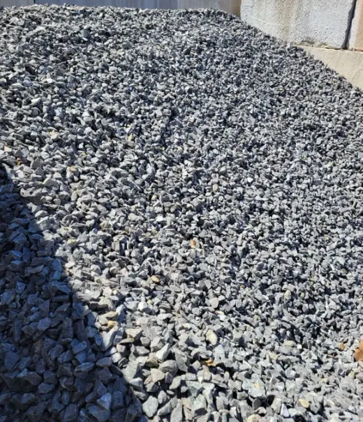 A large pile of uniform, grey crushed stone or gravel with a bright shadow cast across the lower left corner.