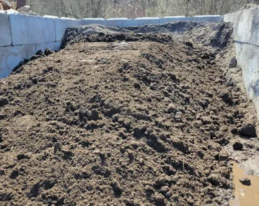 A large pile of dark, coarse soil or compost contained within a concrete bunker.