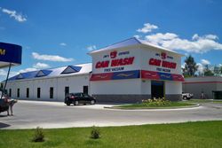 Car dealership building with red signage under a blue sky, with a parked black car in front. Car dealership building with red signage under a blue sky, with a parked black car in front.