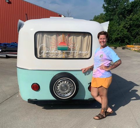 Woman posing beside a mint-and-white teardrop camper with a window curtain and spare wheel. Woman posing beside a mint-and-white teardrop camper with a window curtain and spare wheel.
