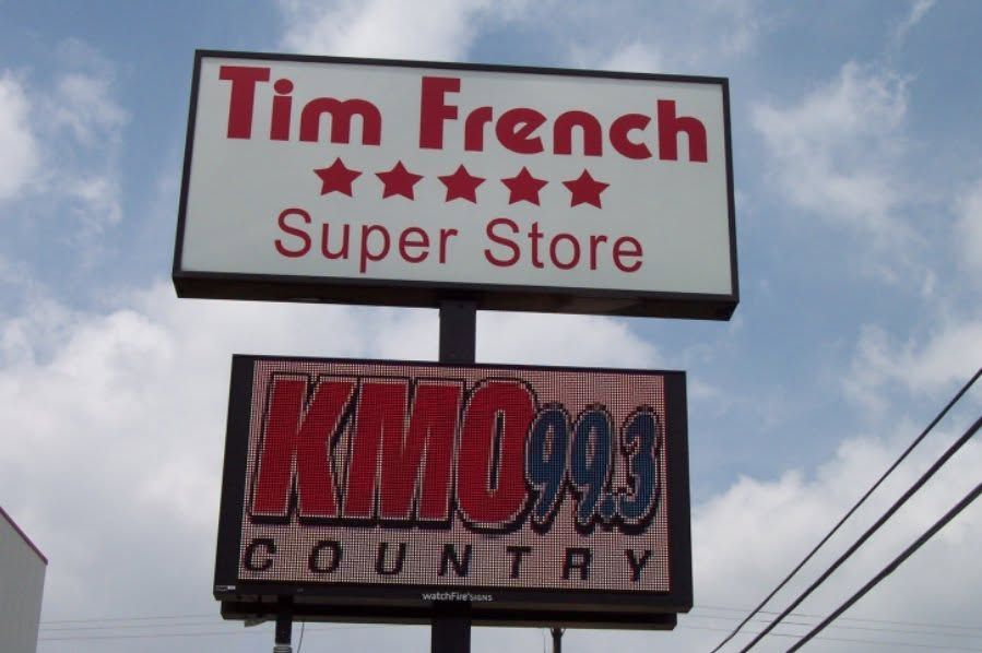 Signs for Tim French Super Store and KMOX 1120 Country against a cloudy sky.