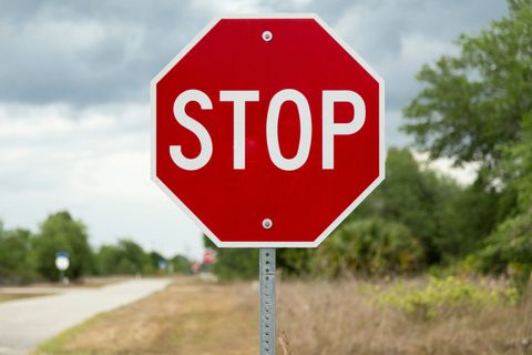 Red stop sign on a rural roadside with trees and cloudy sky in the background. Red stop sign on a rural roadside with trees and cloudy sky in the background.
