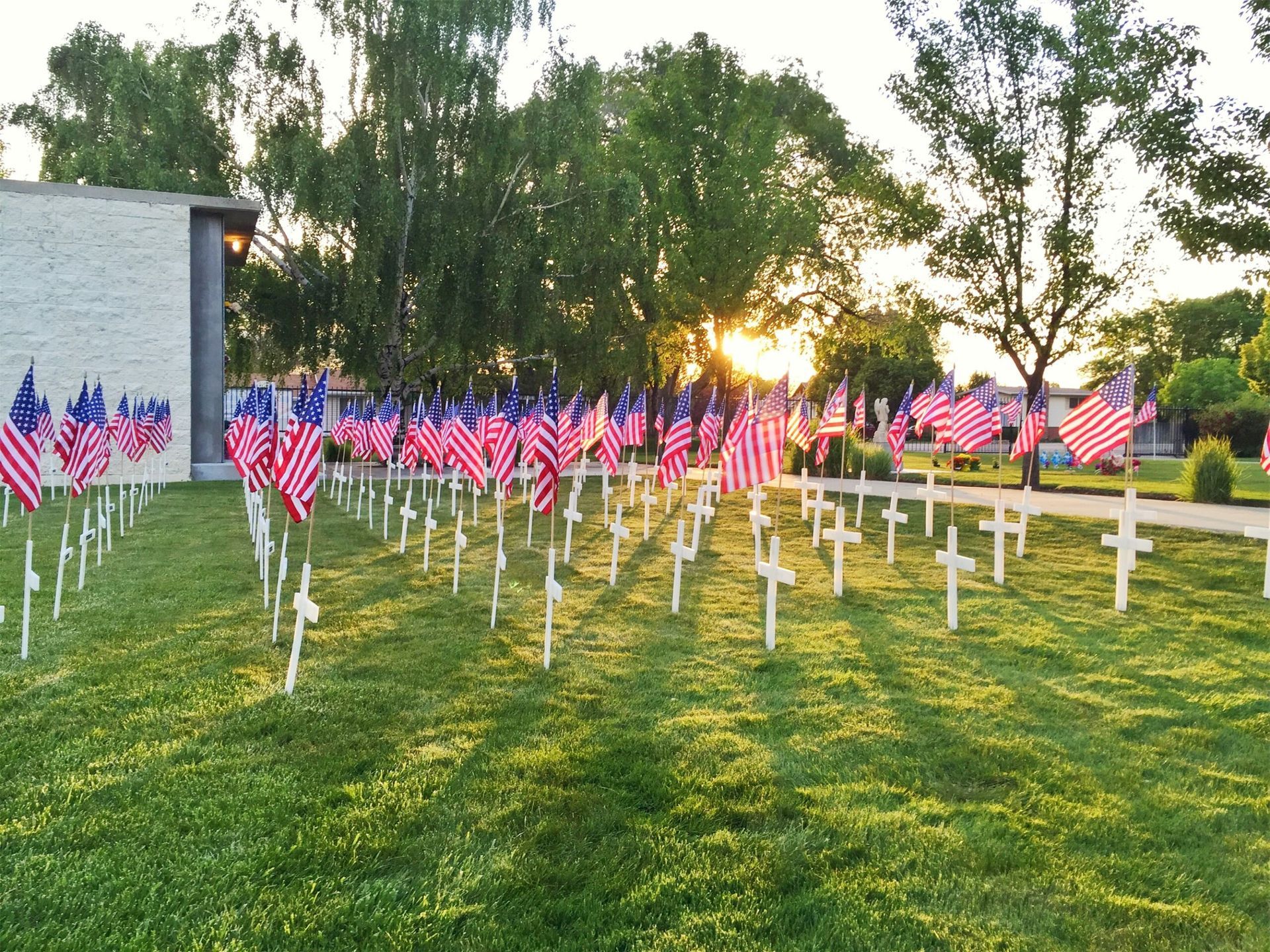 Field of American flags and white crosses, likely a memorial or cemetery. Evening sunlight.