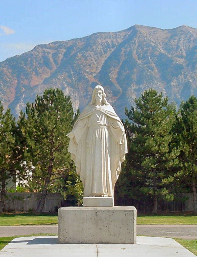 Statue of Jesus with outstretched arms, set against a mountain backdrop and trees.