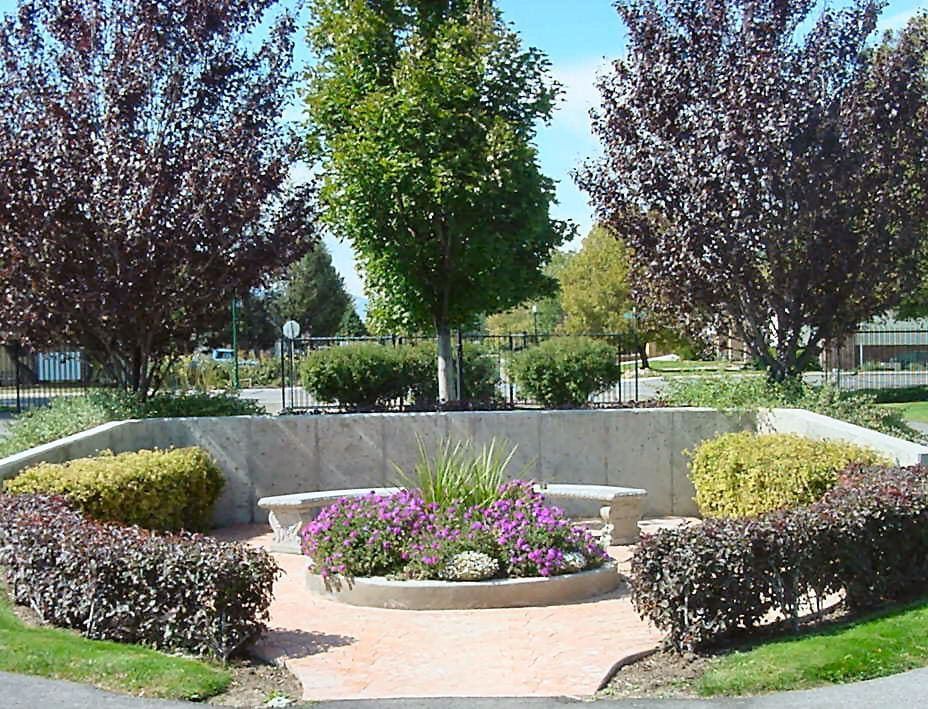 Park with flower bed, benches, and trees in a stone enclosure; trees have red and green leaves.