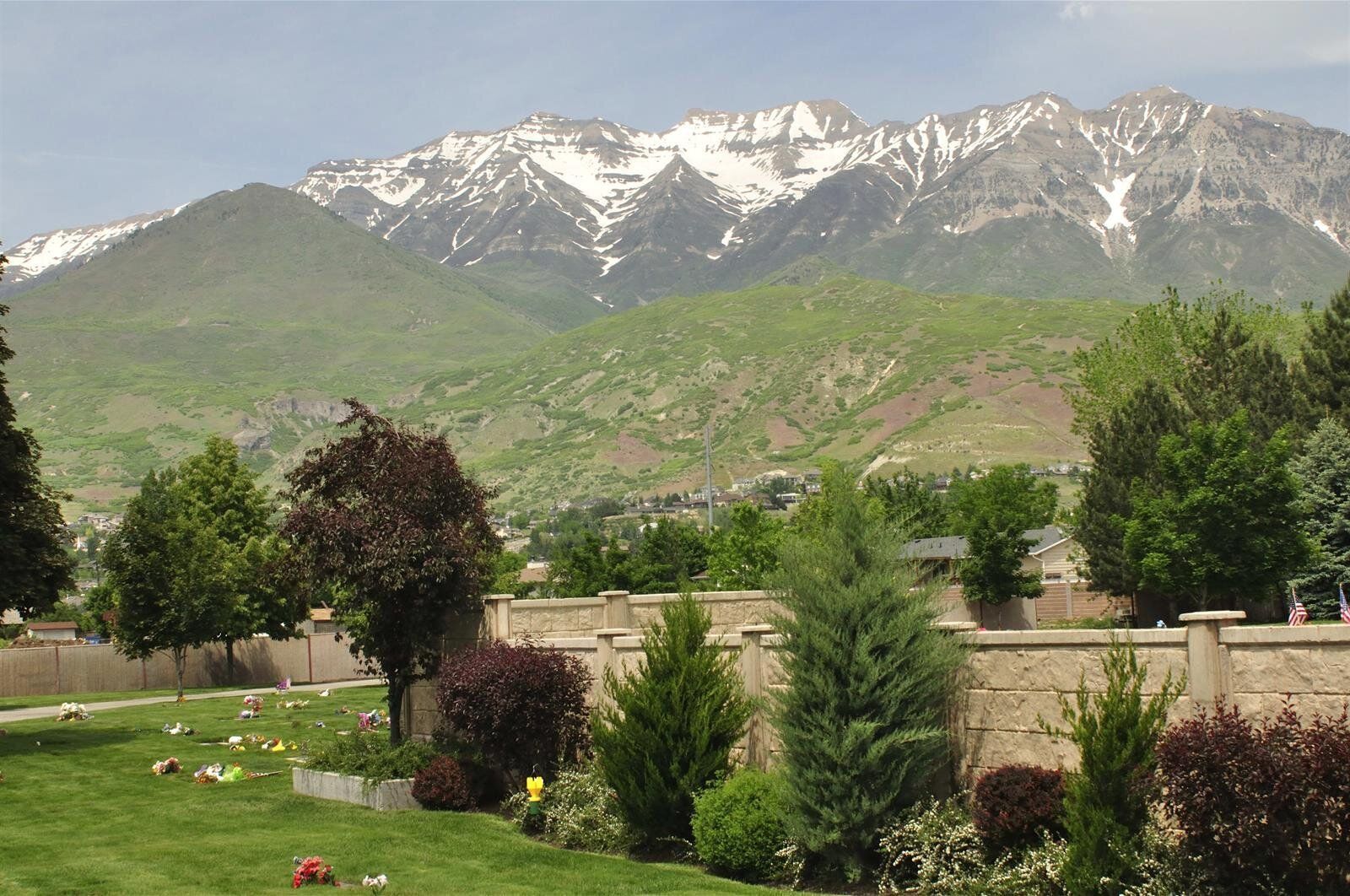 Cemetery with a wall and trees, snow-capped mountains in the background.