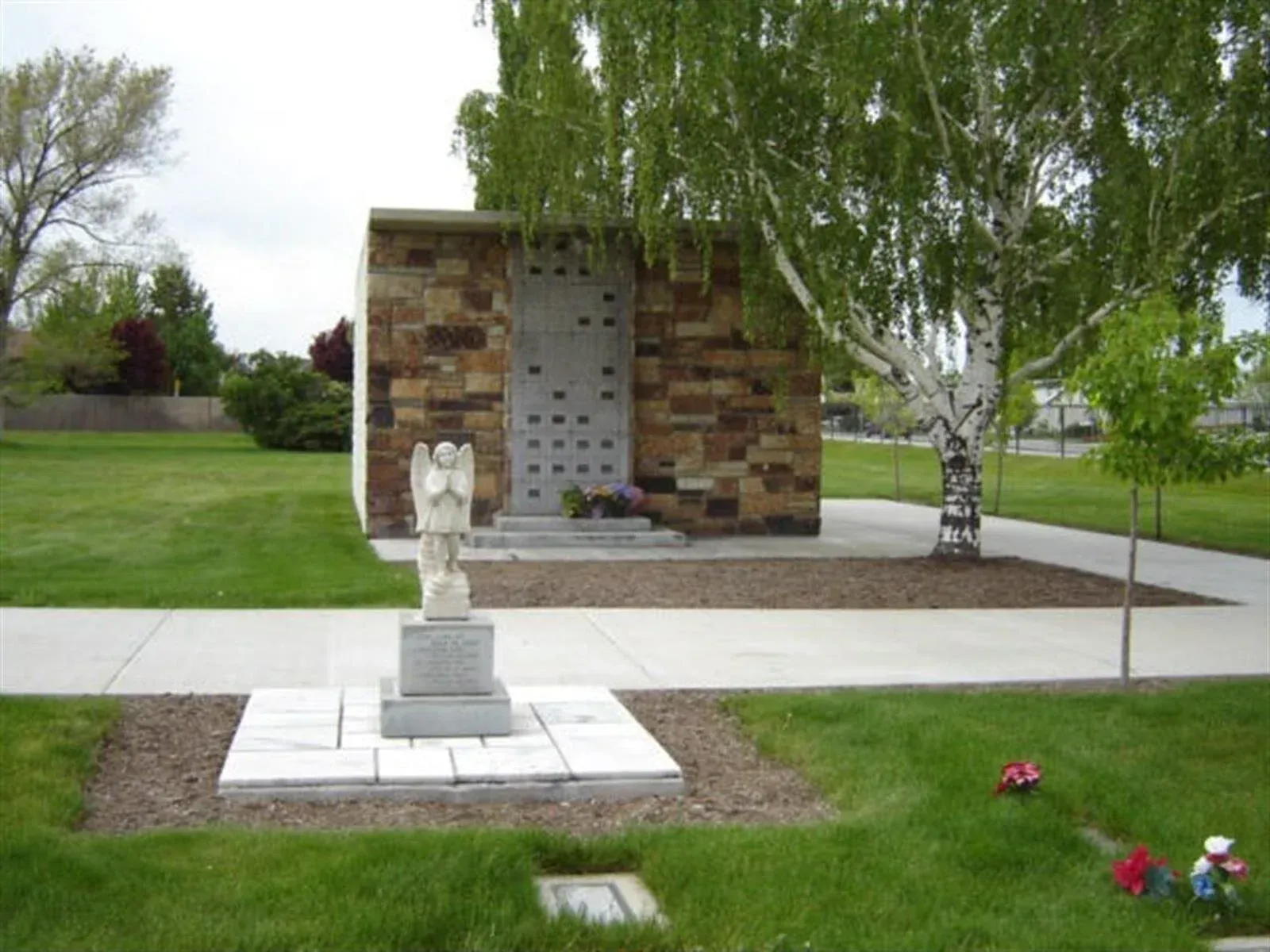 Stone mausoleum in a cemetery with a statue of an angel in front.