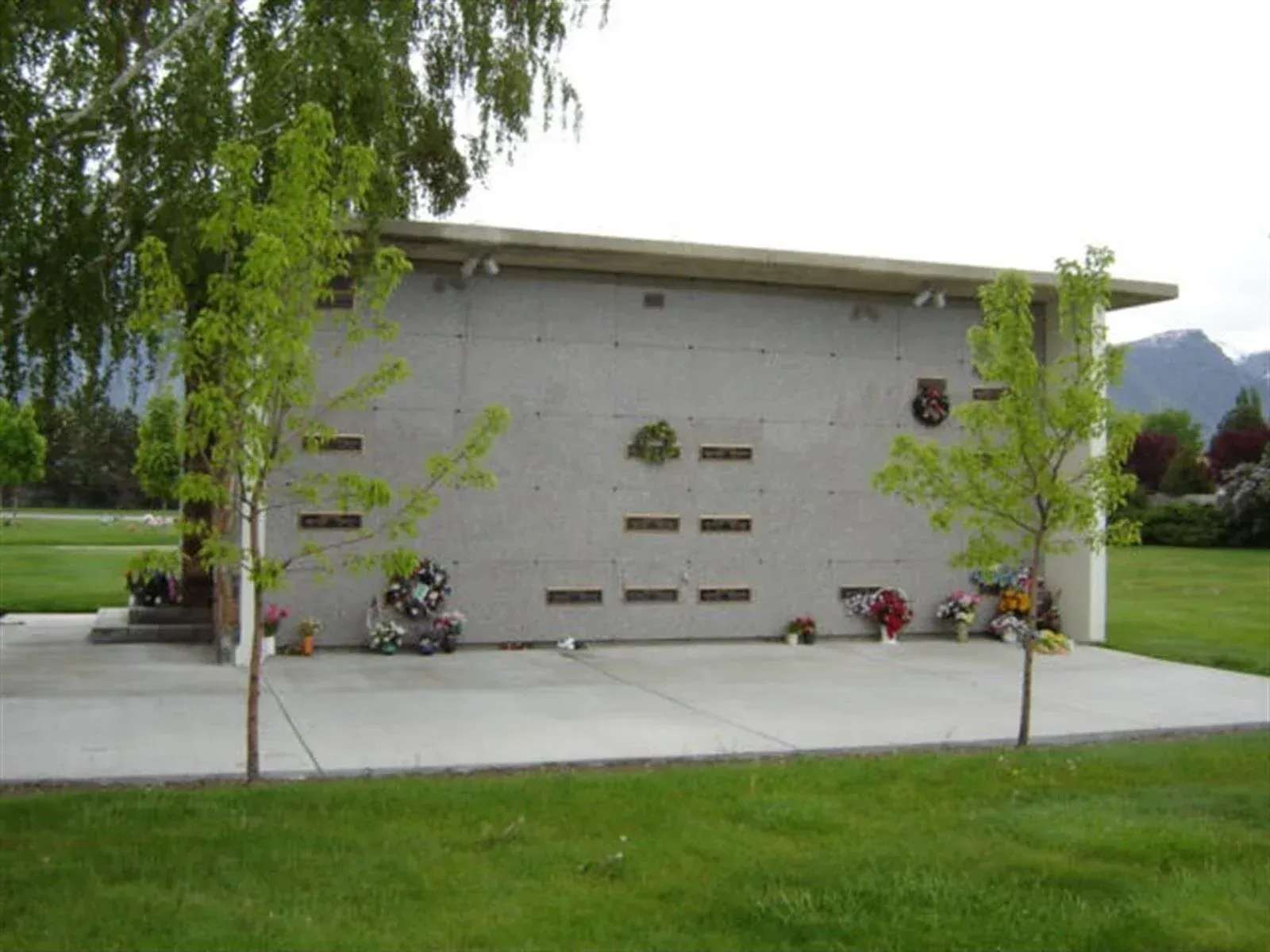 Exterior view of a columbarium with multiple niches, decorated with wreaths and flowers, trees in foreground.