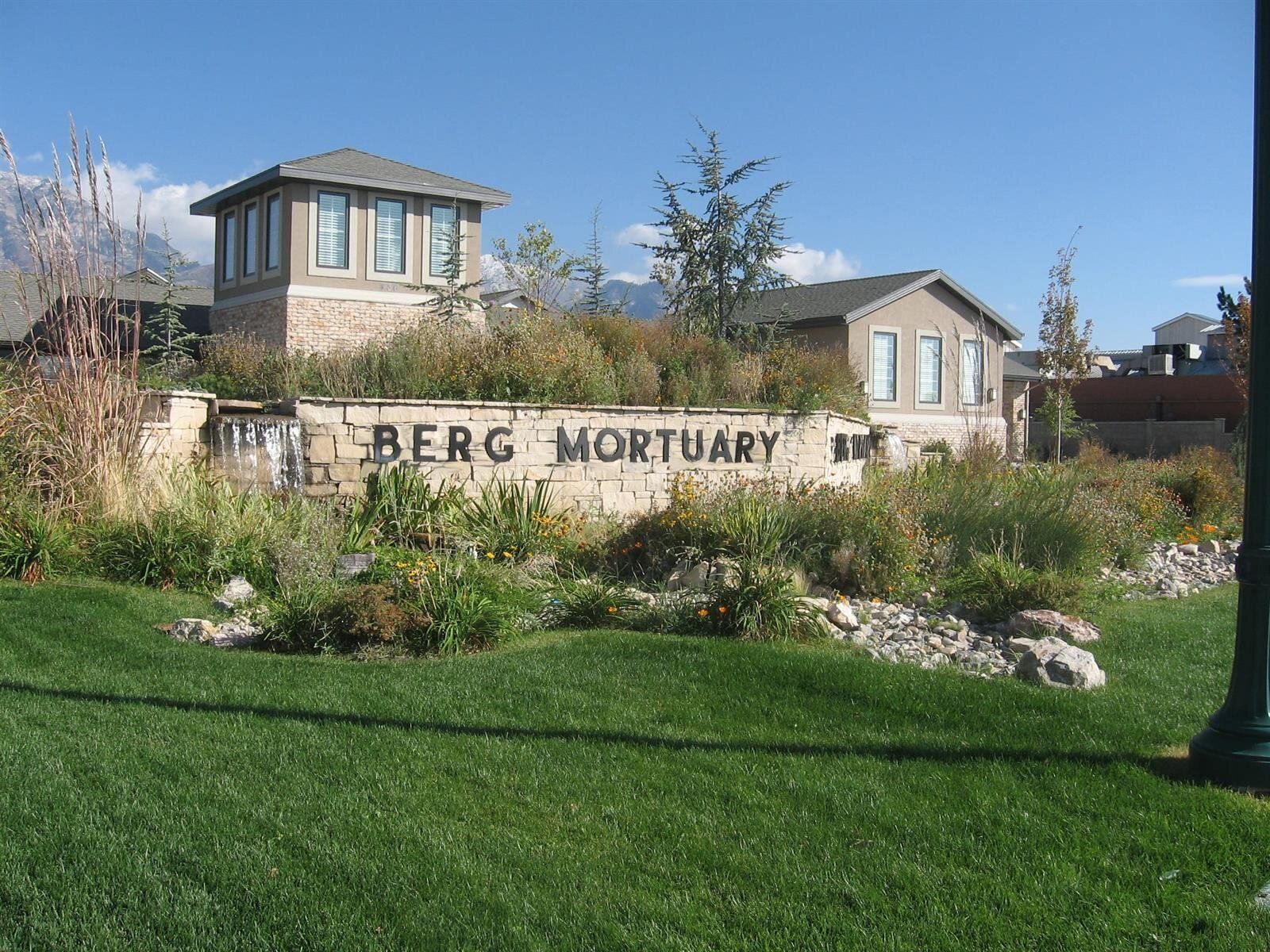 Berg Mortuary sign with stone building, landscaping, and grass.