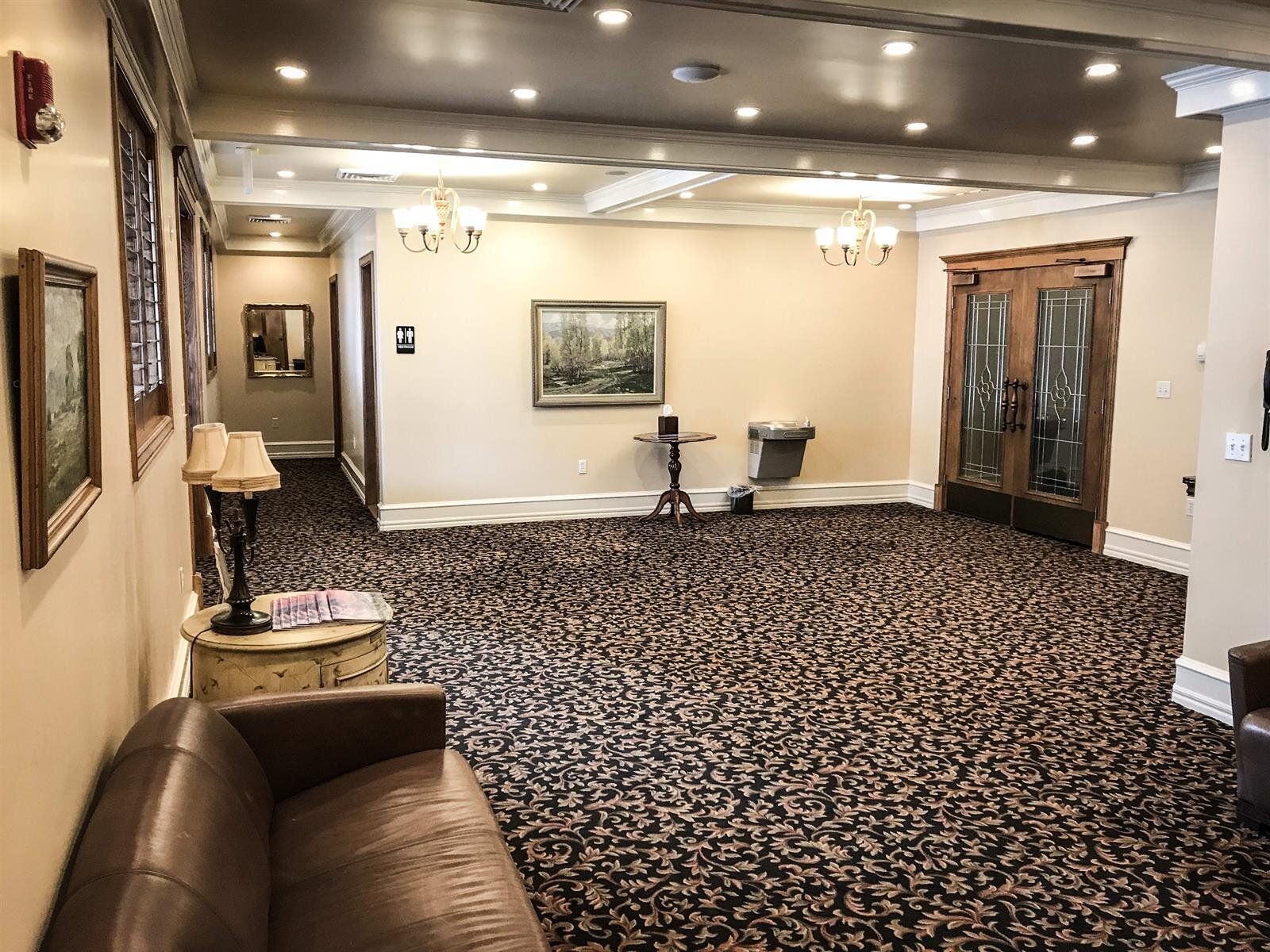 Hallway with patterned carpet, artwork, and double doors. Brown leather sofa on left.