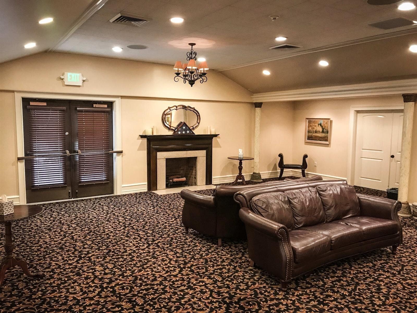 A carpeted room with a fireplace, two leather couches, and double doors.