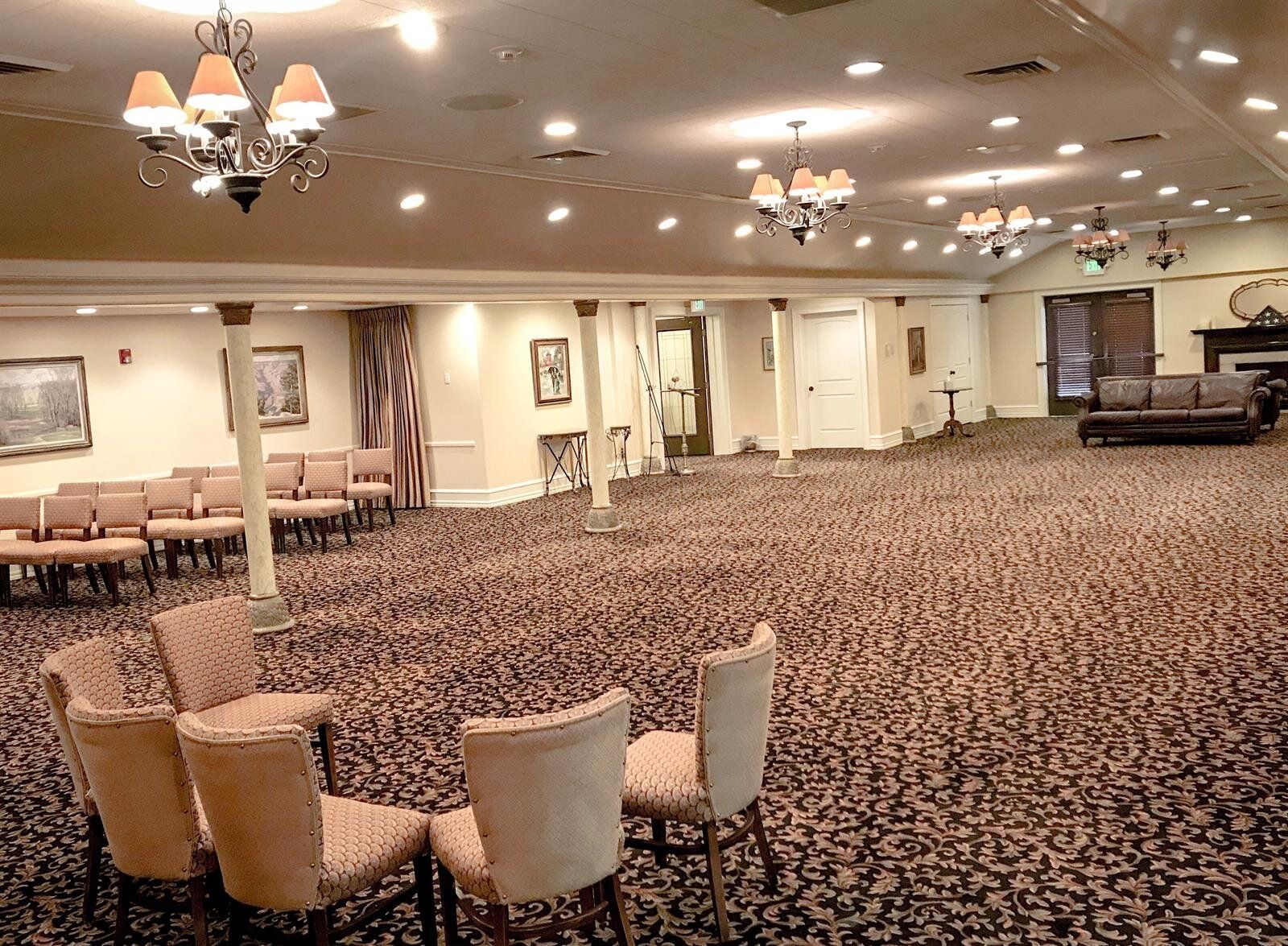Empty reception hall with patterned carpet, chandeliers, and rows of chairs.