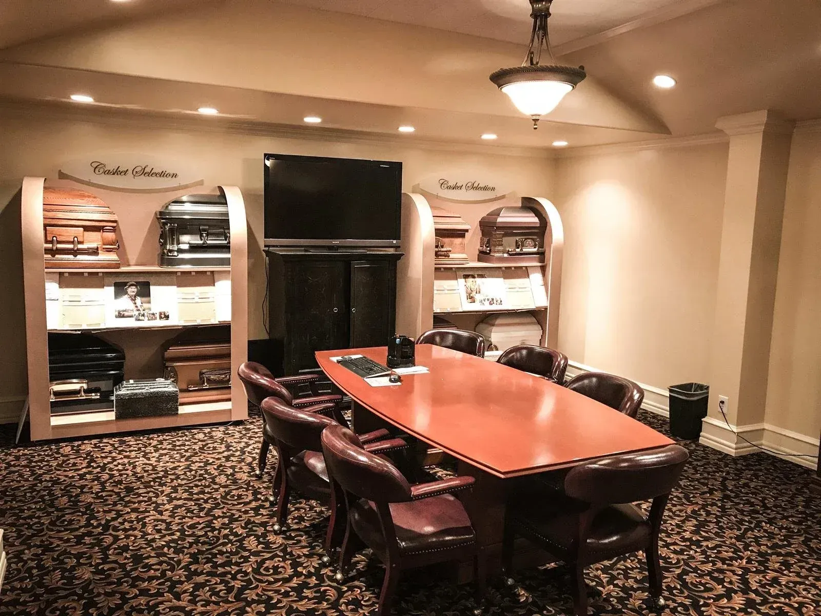 Conference room with large table and chairs. Display shelves, TV, carpet, and neutral walls.
