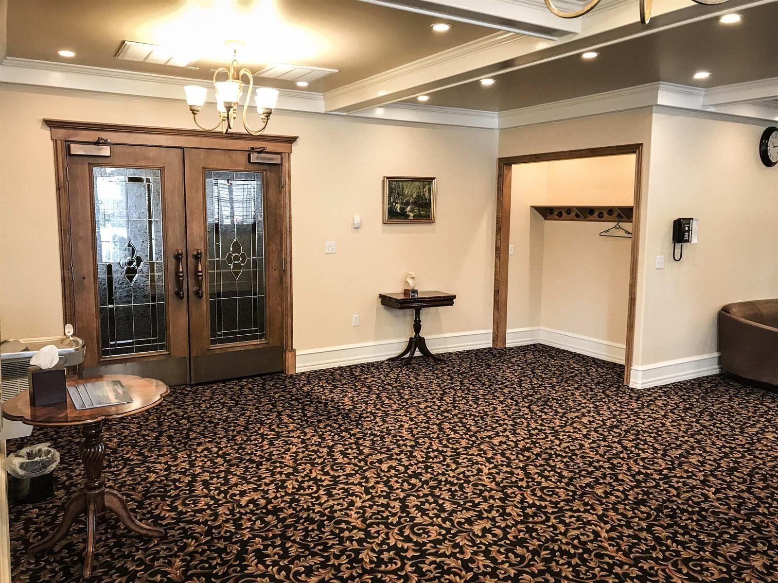 Elegant room with wood-framed doors, patterned carpet, small table, and coat rack.