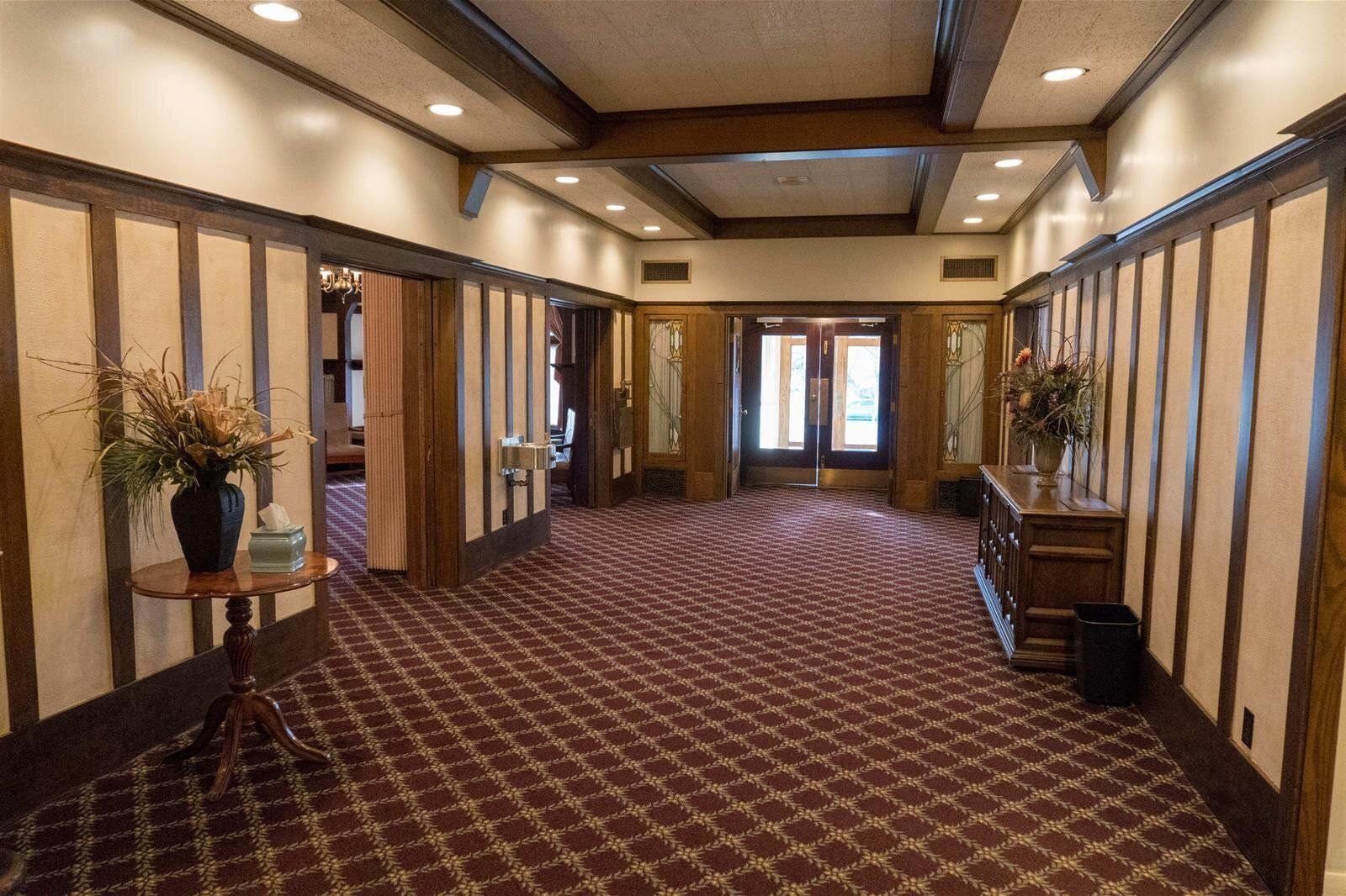 Hallway with brown paneled walls, patterned carpet, and wooden beams.