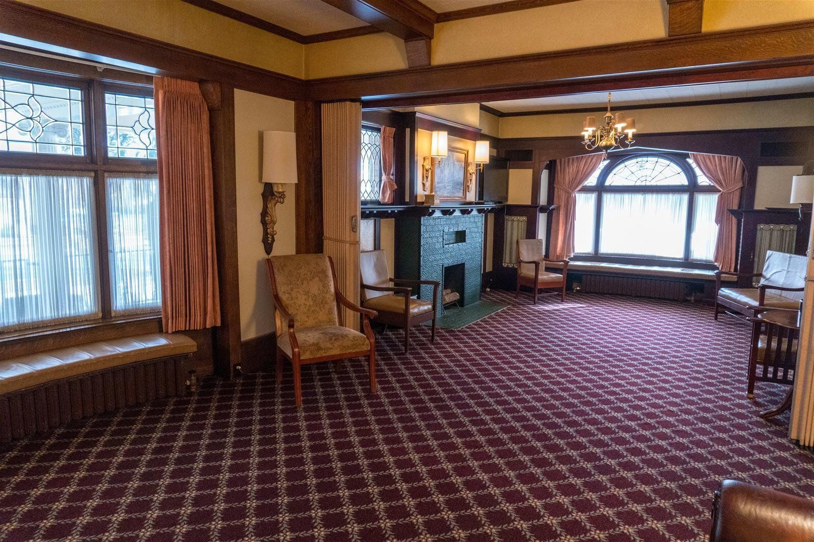 Room with red patterned carpet, dark wood trim, fireplace, and arched windows.