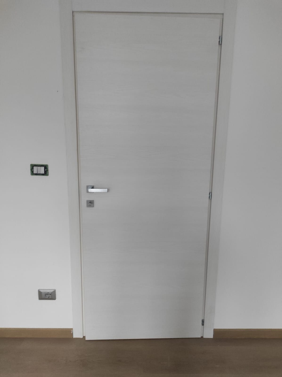 Una porta bianca si trova in una stanza accanto a un muro bianco.