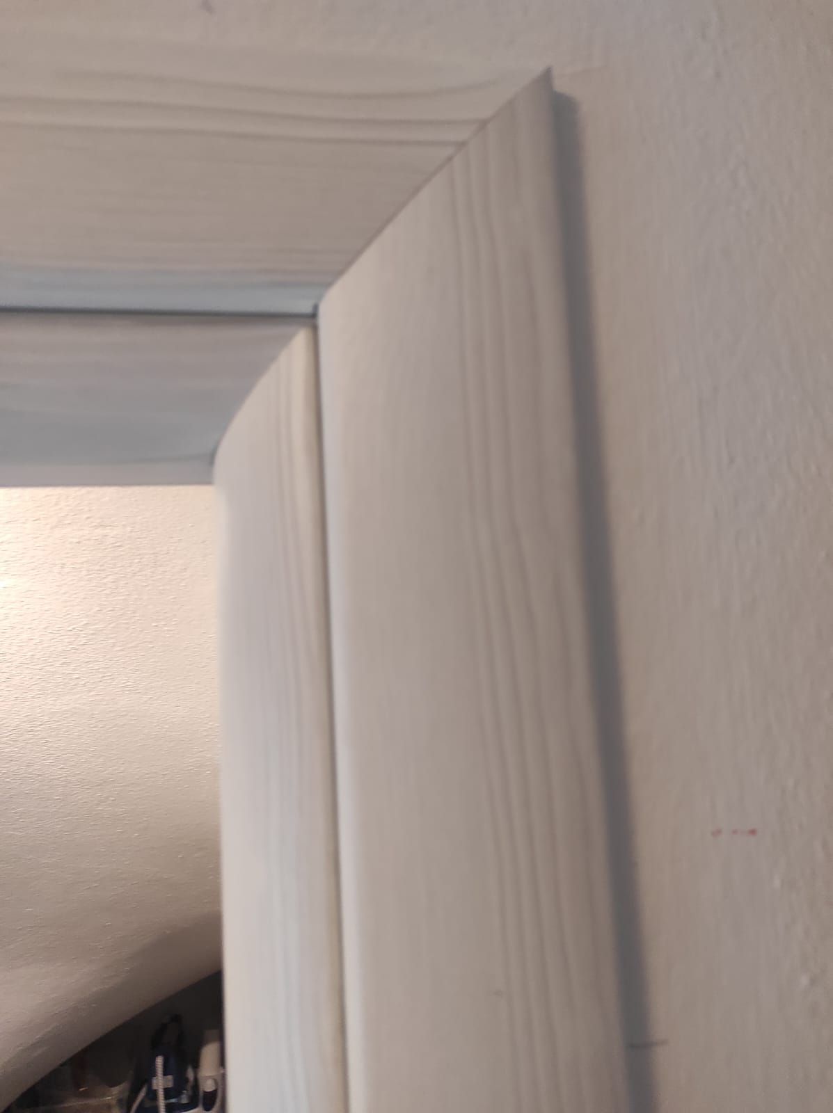 Un primo piano dello stipite di una porta bianca su una parete bianca.