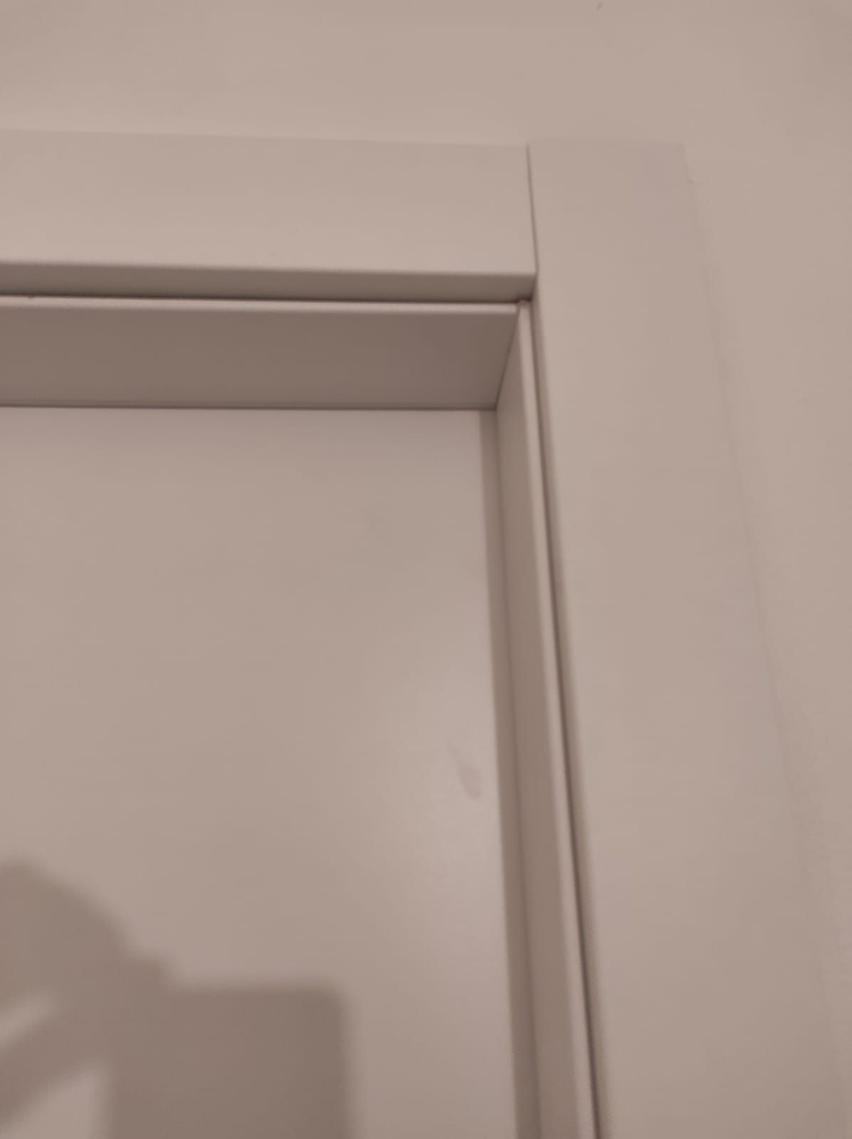 Un primo piano dello stipite di una porta bianca su una parete bianca.