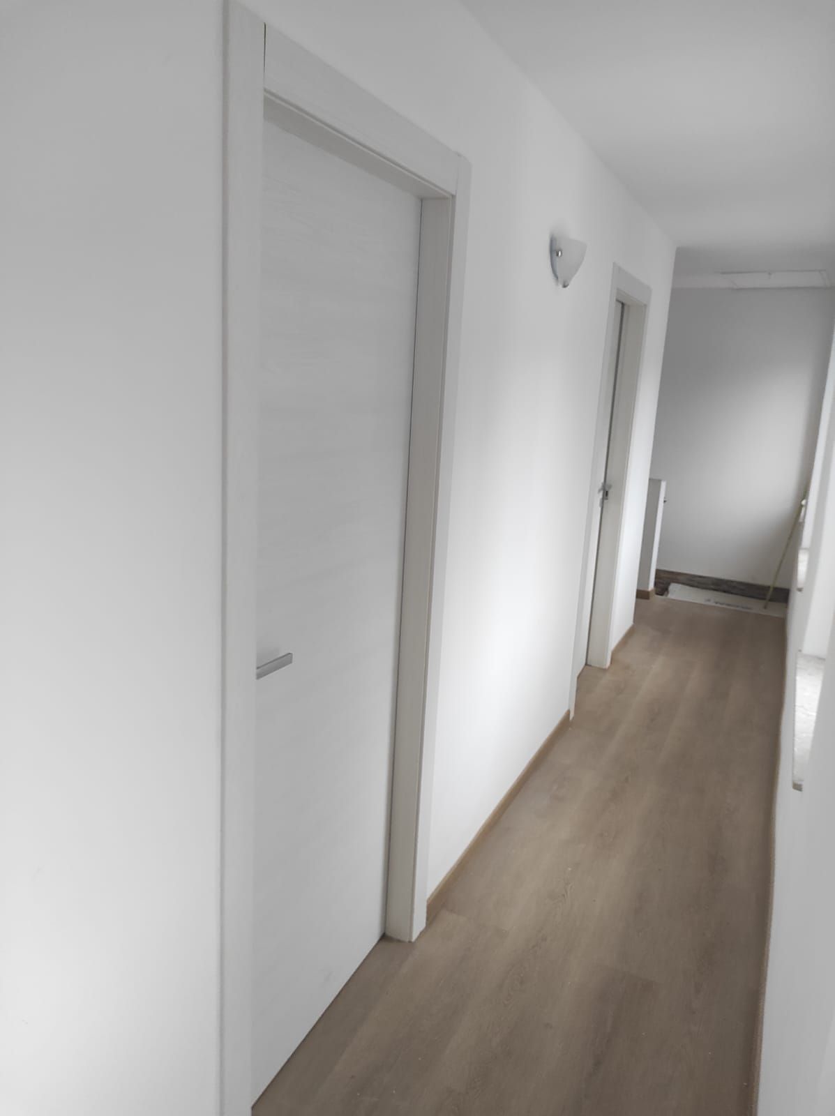 Un lungo corridoio con pareti bianche e pavimenti in legno.