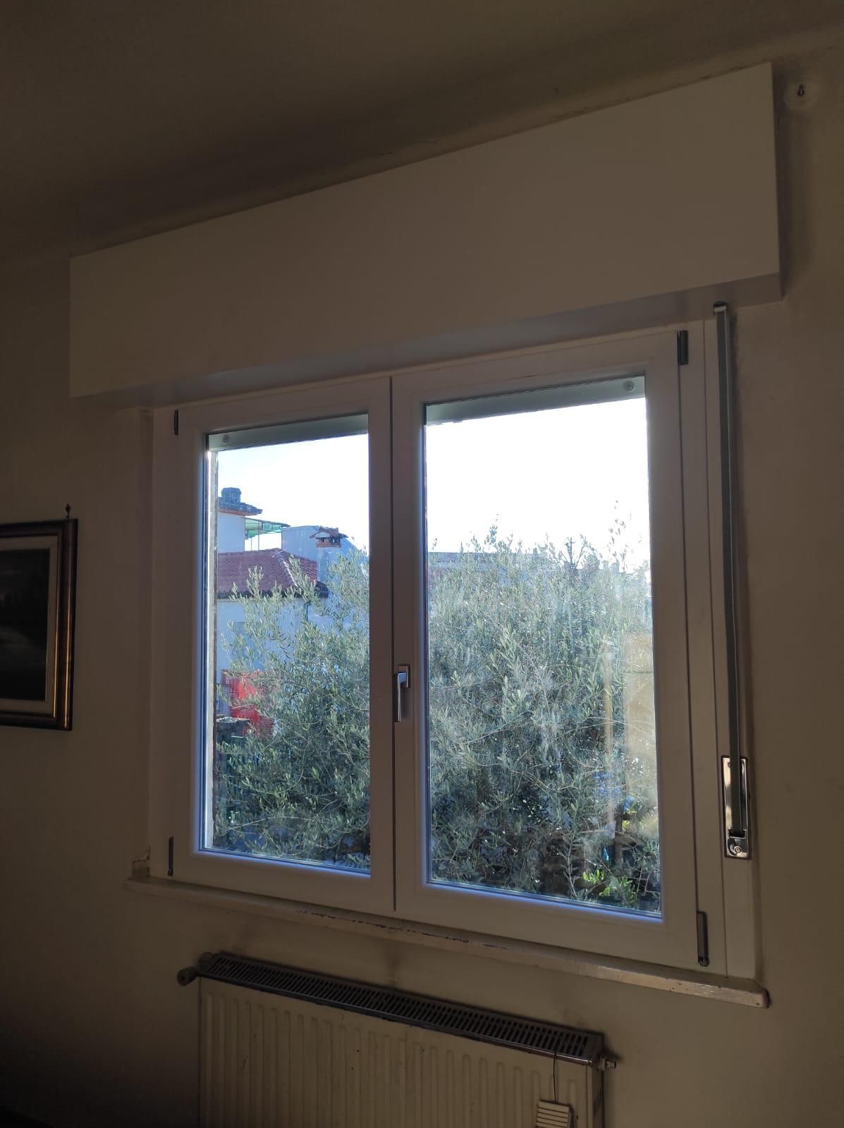 Una stanza con una finestra, un termosifone e un quadro sul muro.