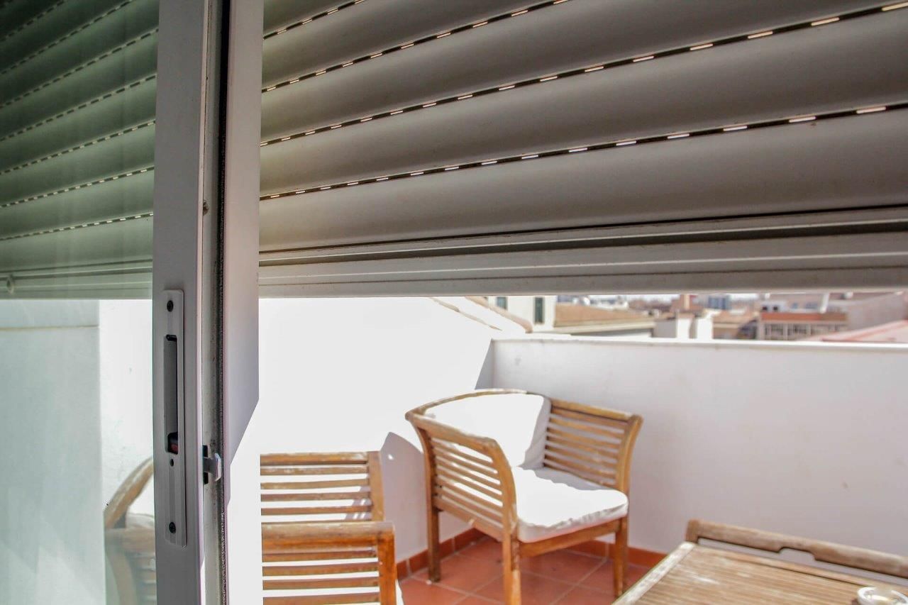 Un balcone con tavolo e sedie e una persiana alla finestra.