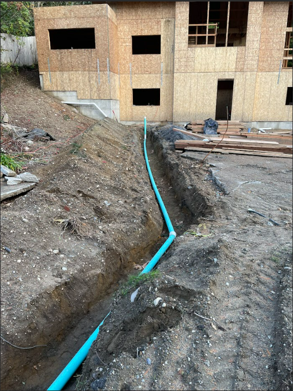 A blue pipe is laying in the dirt in front of a house under construction.