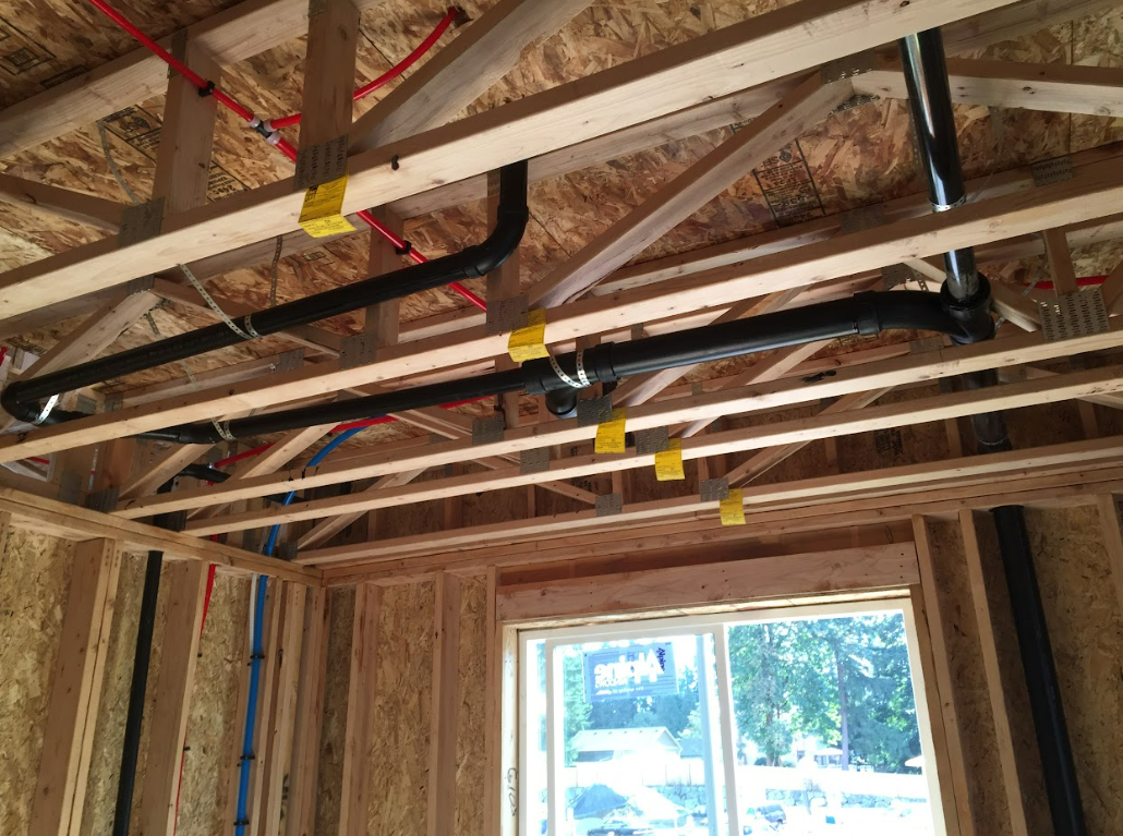 A room under construction with a window and pipes hanging from the ceiling.