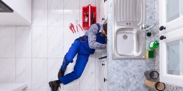 A plumber under a kitchen sink performing repairs