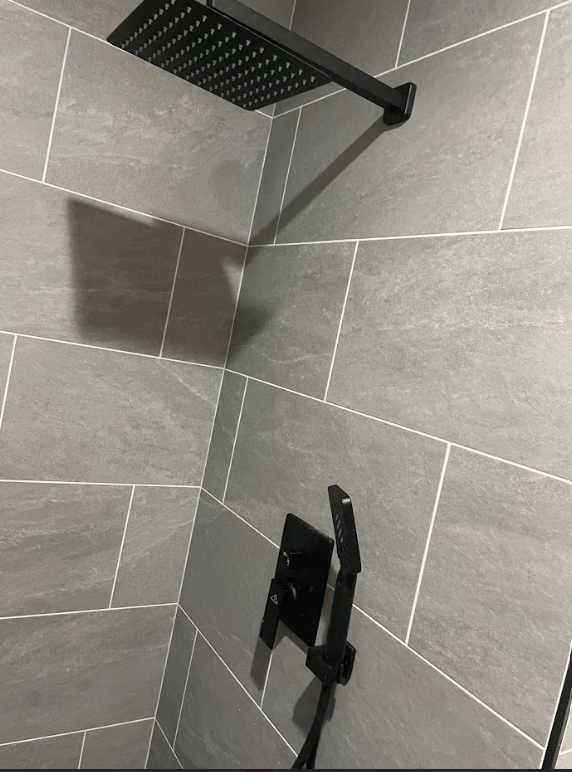 A black shower head is hanging from a tiled wall
