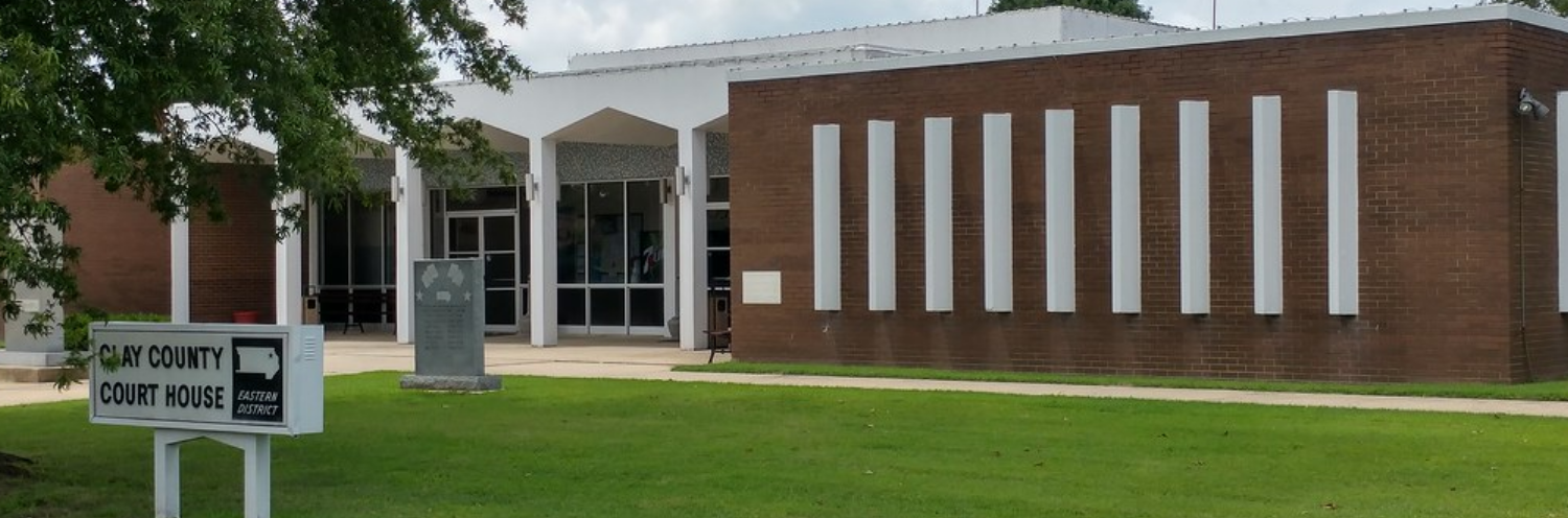 Brick building with white columns and a sign on a green lawn, under cloudy skies