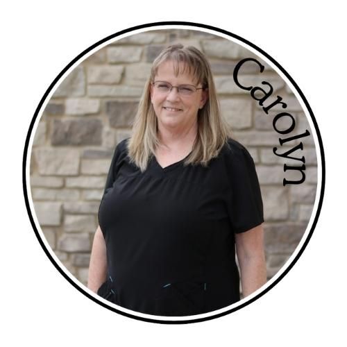 Portrait of Carolyn standing outdoors in a black shirt before a stone wall, with her name on the image