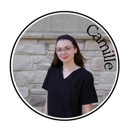 Portrait of a person in glasses wearing a black top against a stone wall, with “Camille” text along the edge