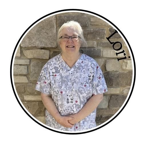 Smiling person in floral scrub top standing before a stone wall, with “Lori” along the edge