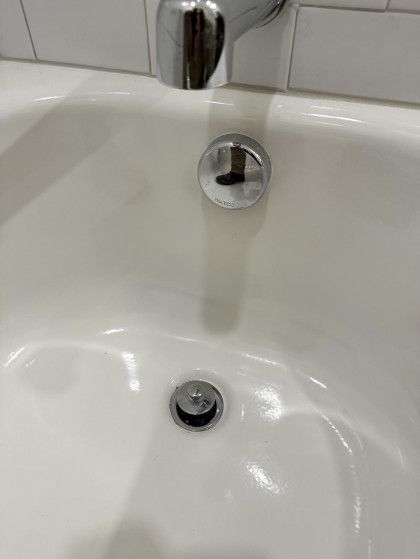 Close-up of a white bathtub with a chrome drain stopper and overflow drain.