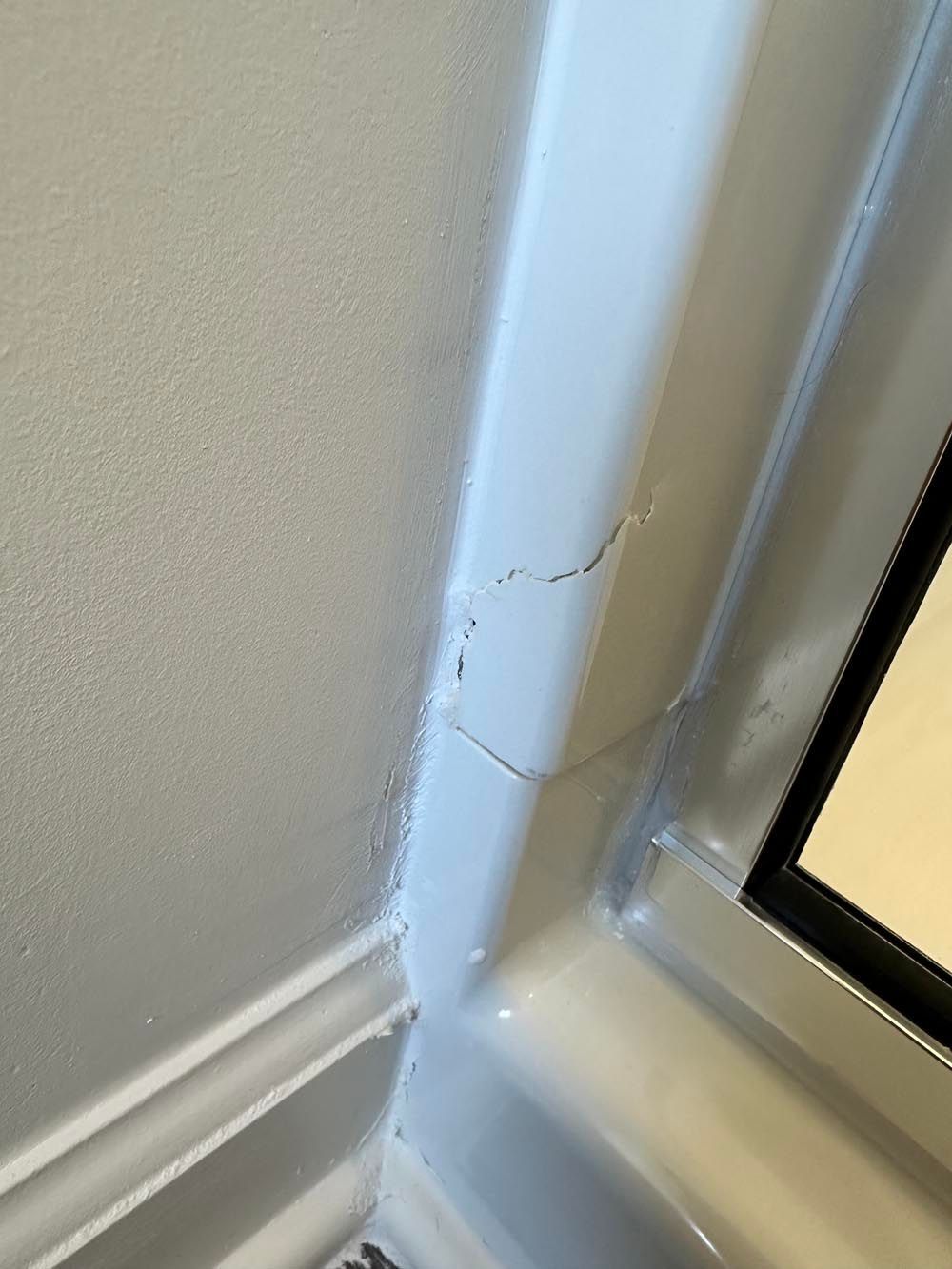 Crack in the white plastic frame of a shower door against a painted wall.