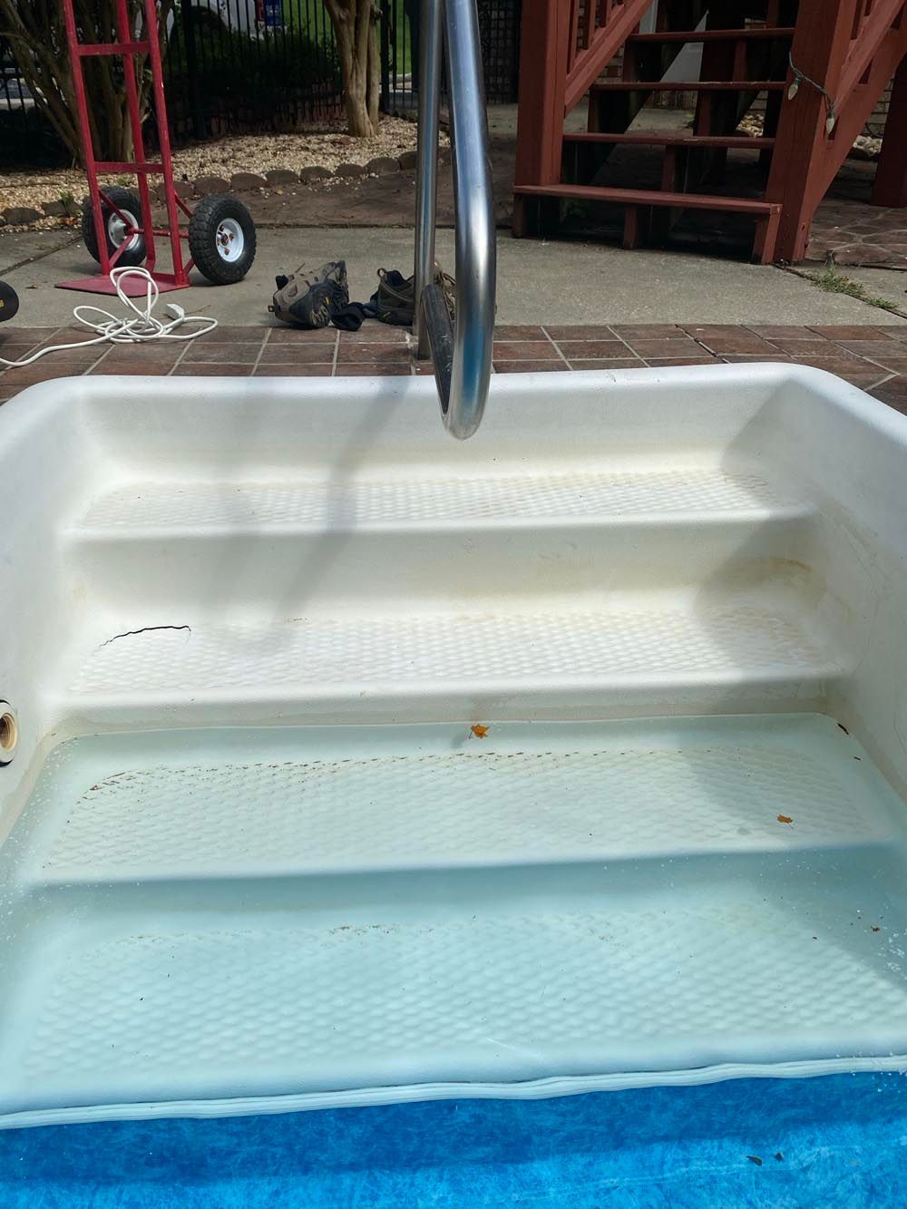 Steps leading into a small pool with handrail. Water is a light blue, pool's sides and steps are white.