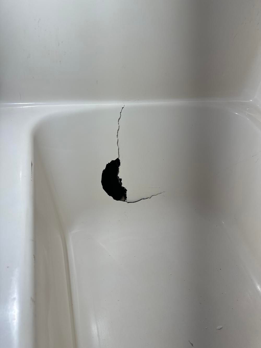 White bathtub with a large hole and cracks in the bottom.