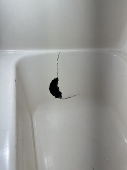 White bathtub with a large, dark hole and cracks in the bottom.